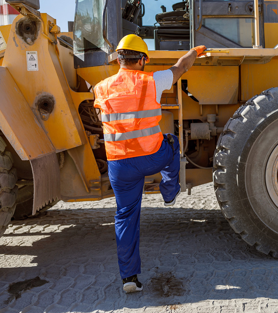 A foreman wearing a hard hat climbing onto construction equipment.